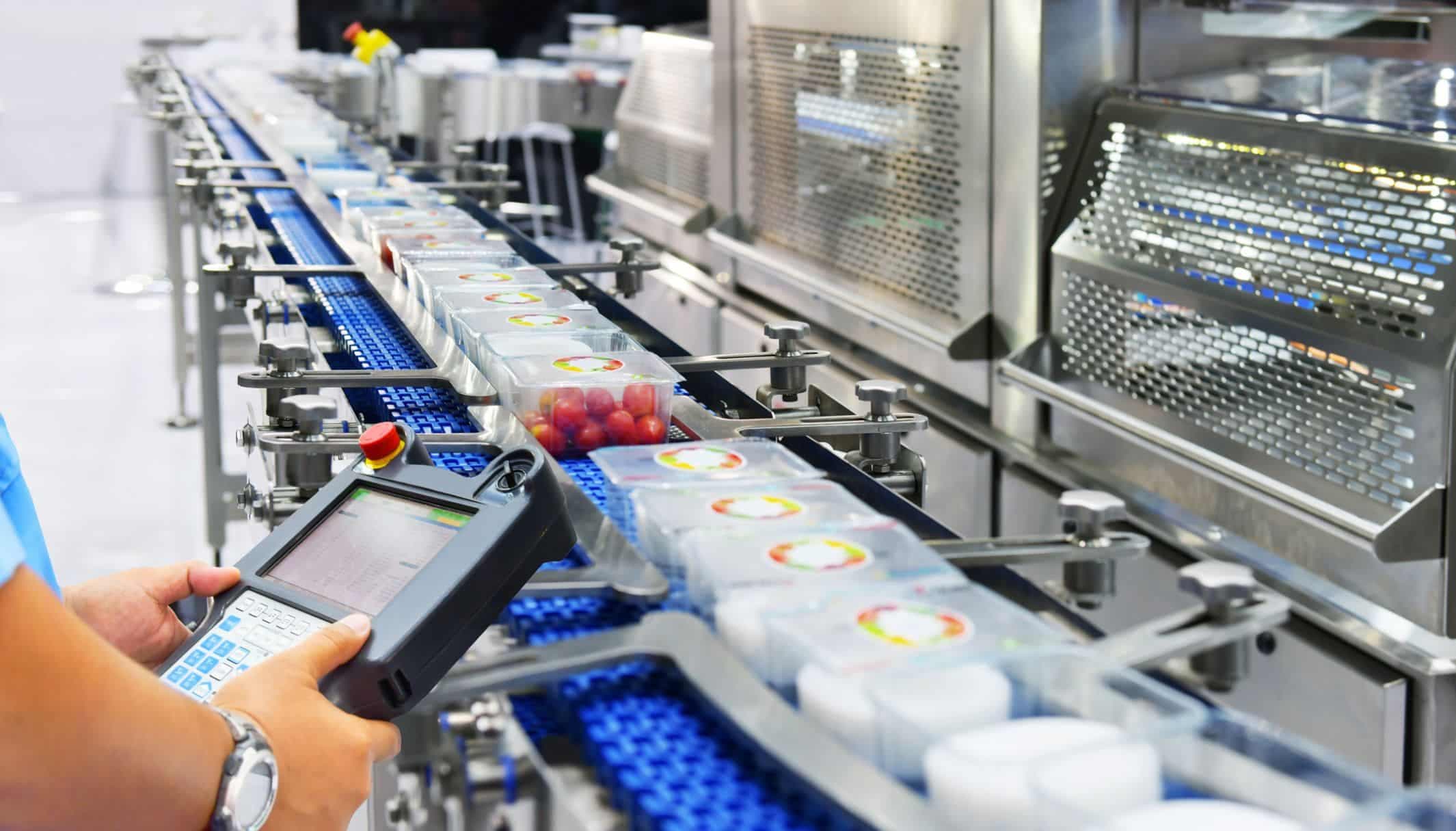 An operator with a handheld terminal beside a packaging line carrying sealed tubs.