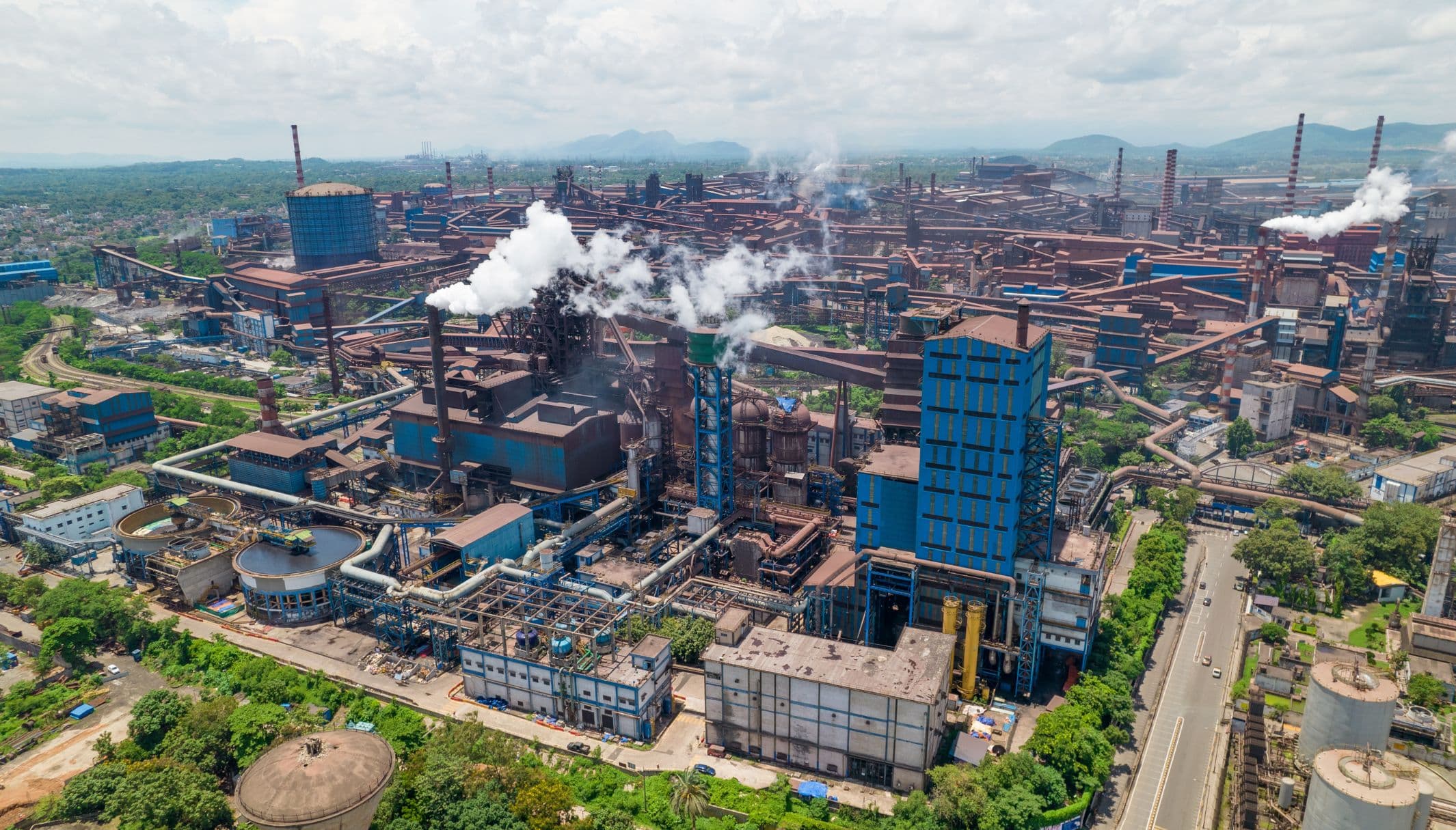 Aerial view of a steel works, with smoke rising from its stacks.