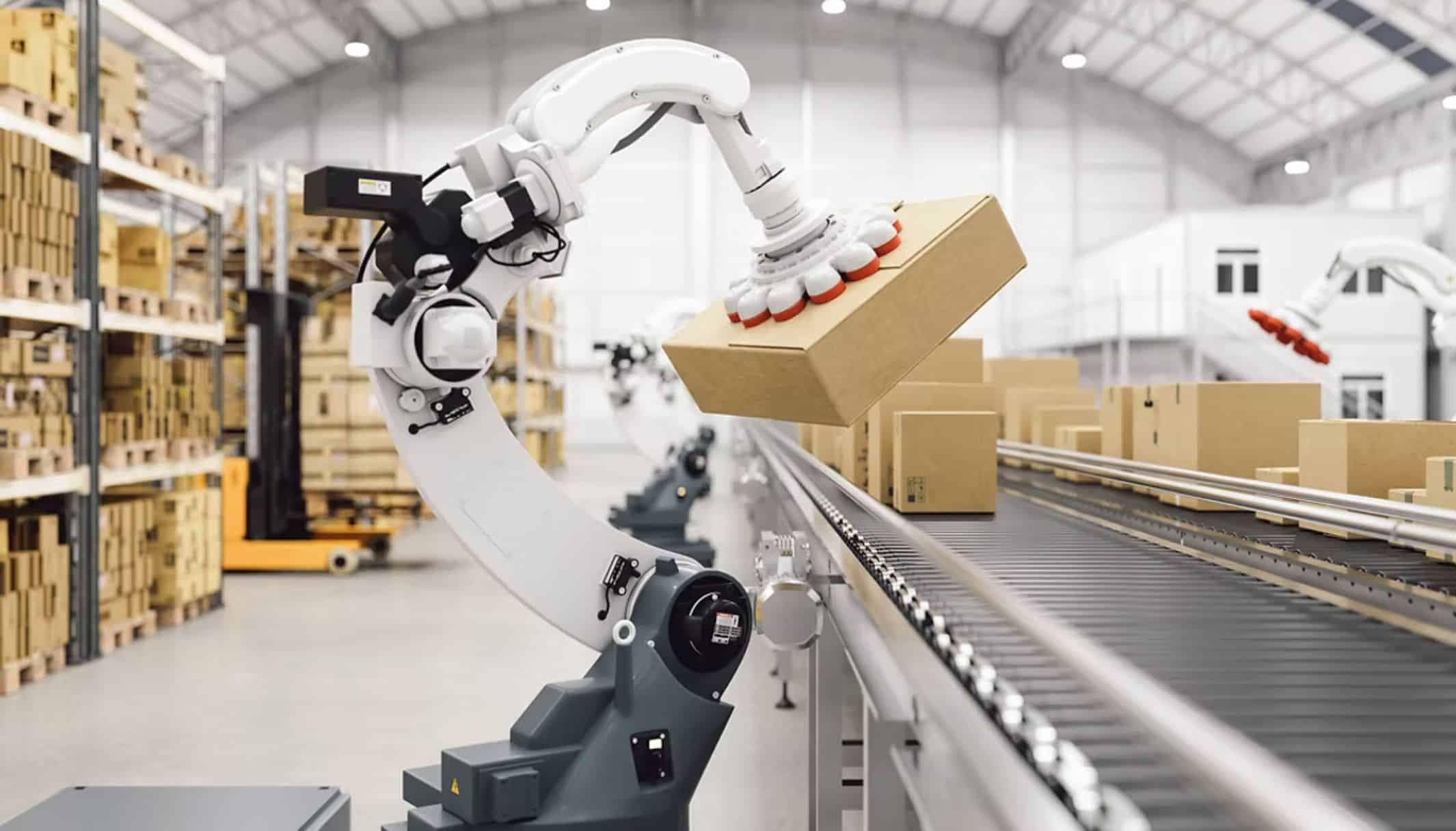 A robot arm with a suction gripper lifting a cardboard box onto a conveyor in a warehouse.