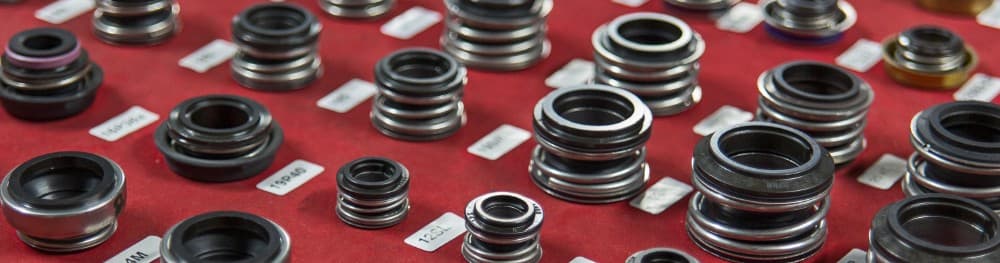 Dozens of mechanical face seals laid out in labelled rows on a red inspection surface.