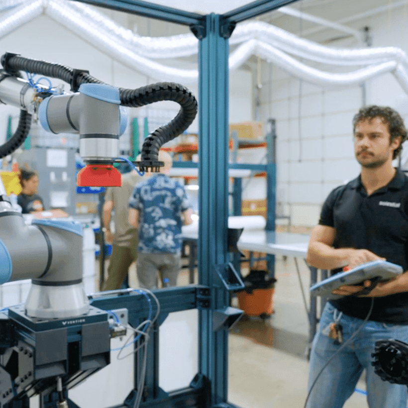 An engineer holding a tablet beside a collaborative robot arm on a production bench.