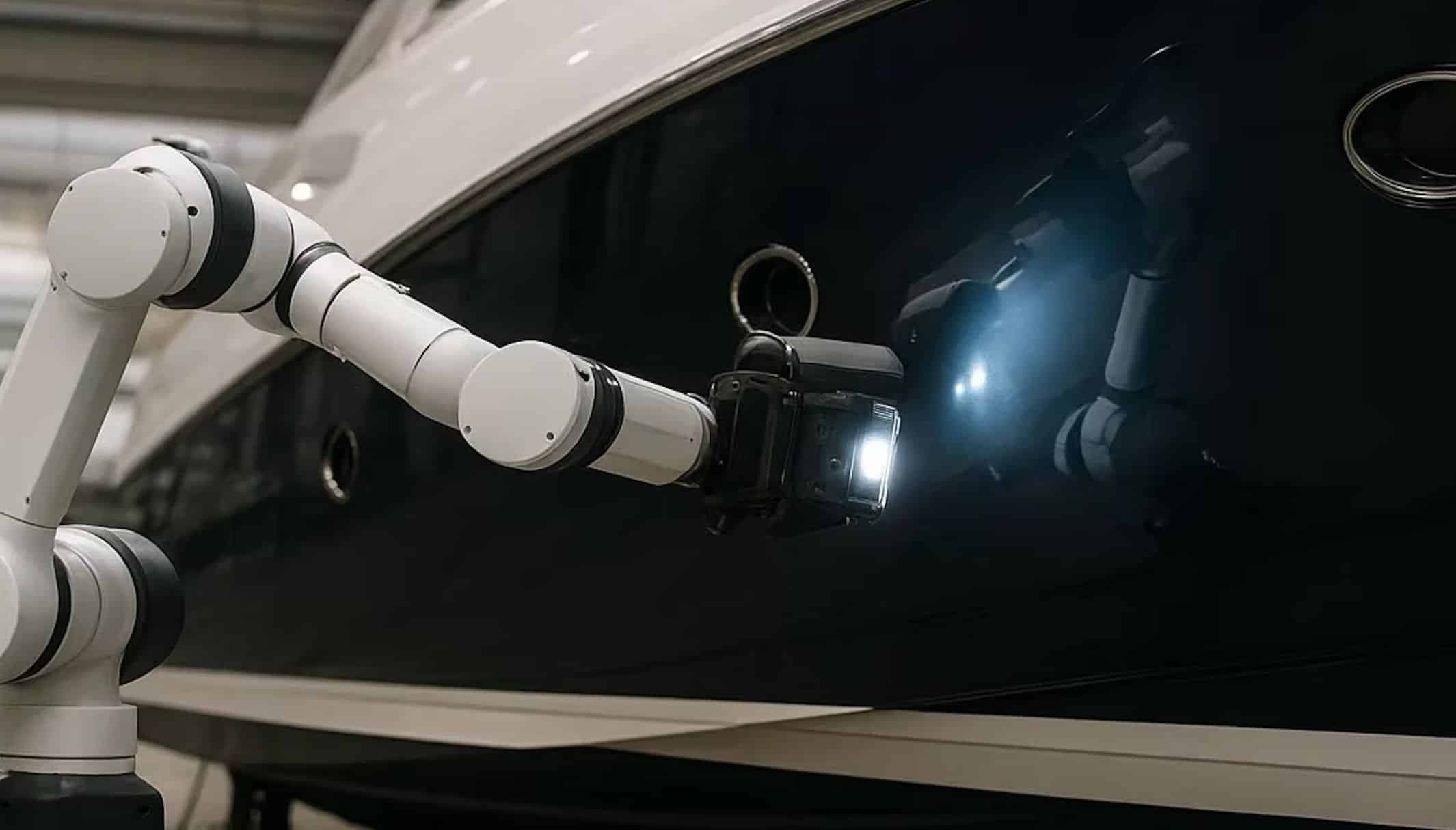 A robot arm with a camera and lamp inspecting the dark hull of a yacht.