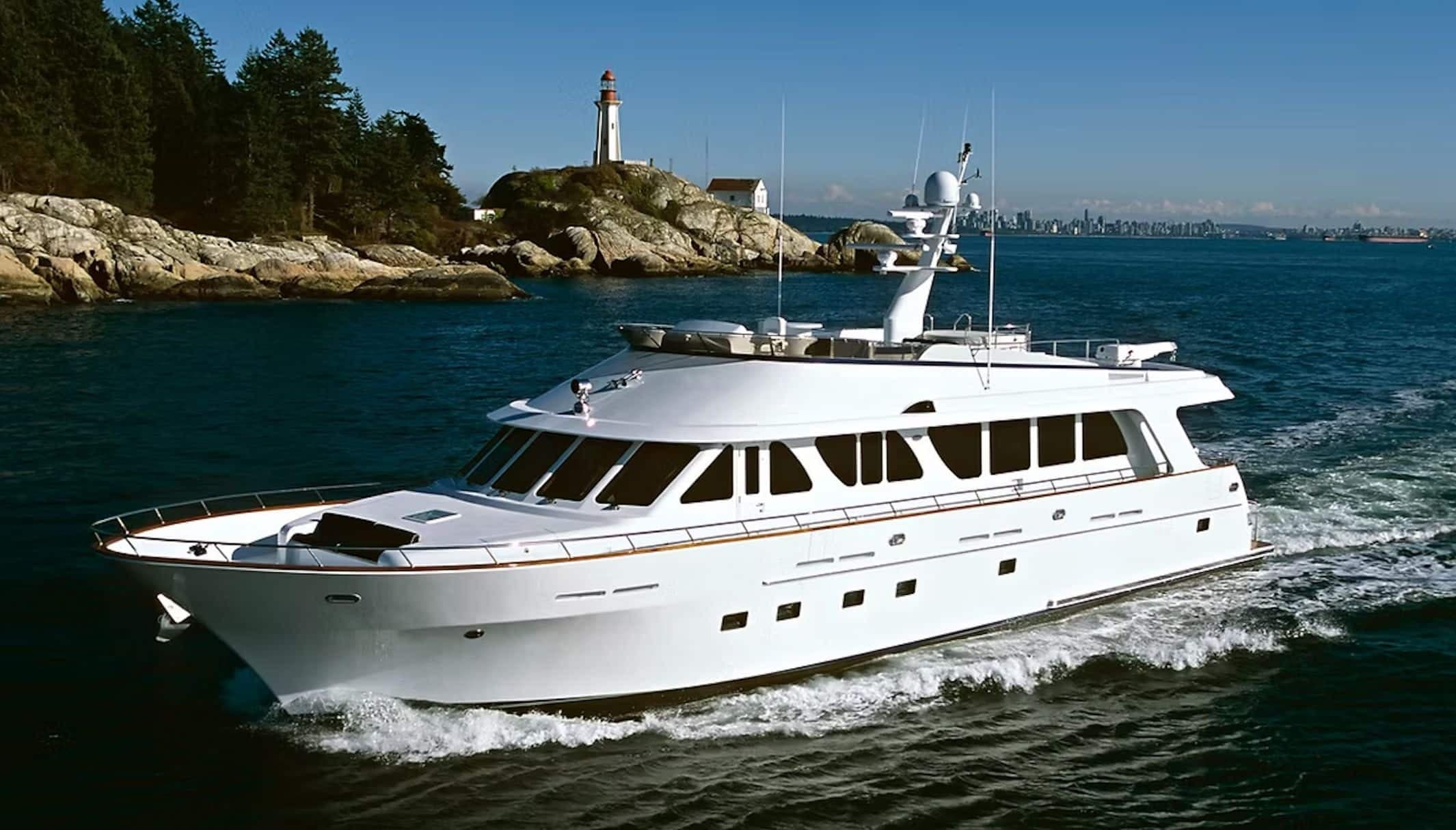A white motor yacht underway past a rocky headland and lighthouse.